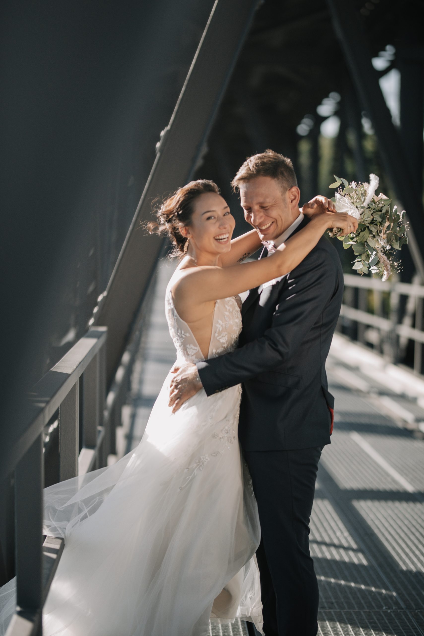 Brautpaar hat einen intimen Moment auf achitektonischer Brücke, beide lachen herzhaft