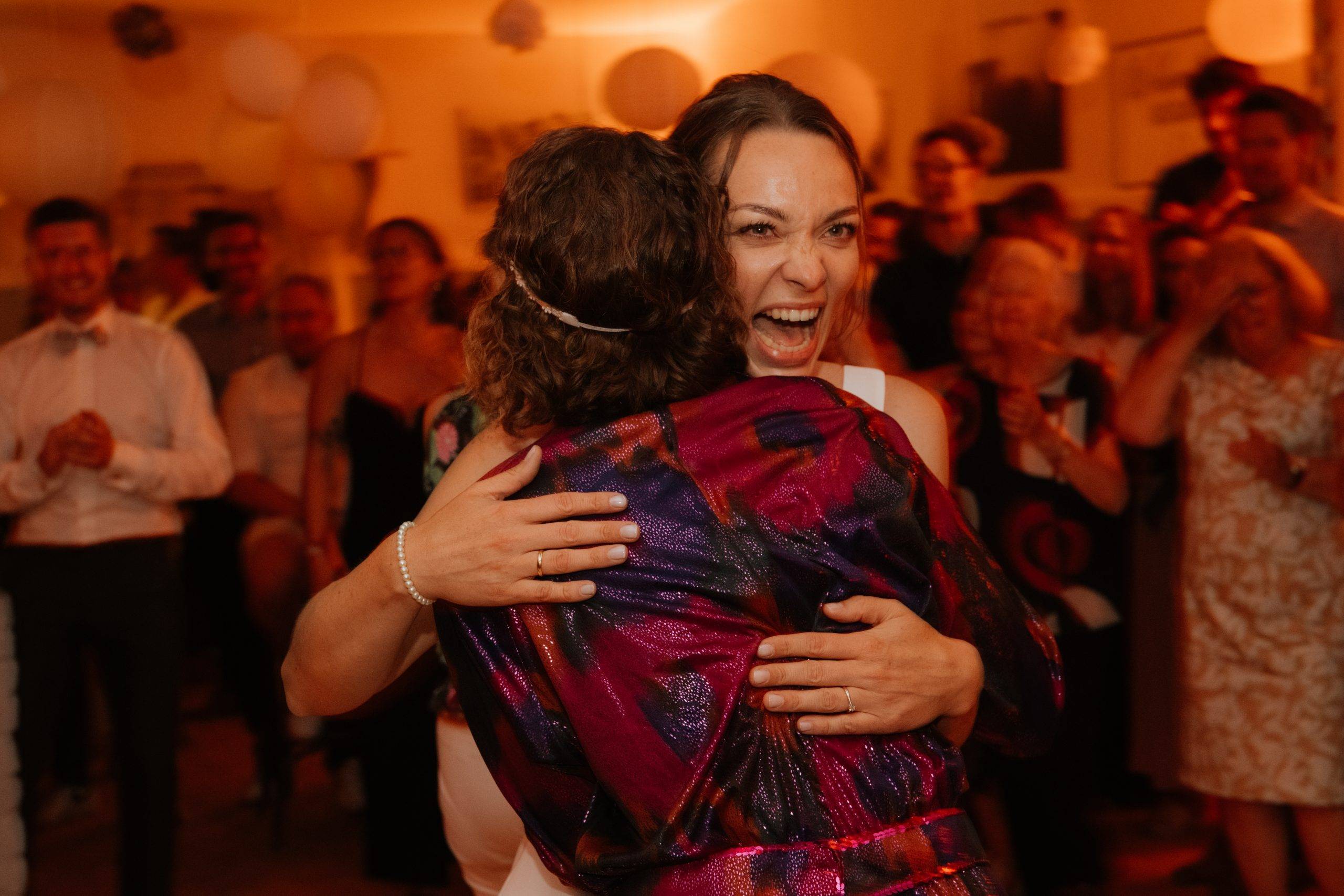 Braut umarmt Trauzeugin mit guter Laune, sehr emotionales Partybild