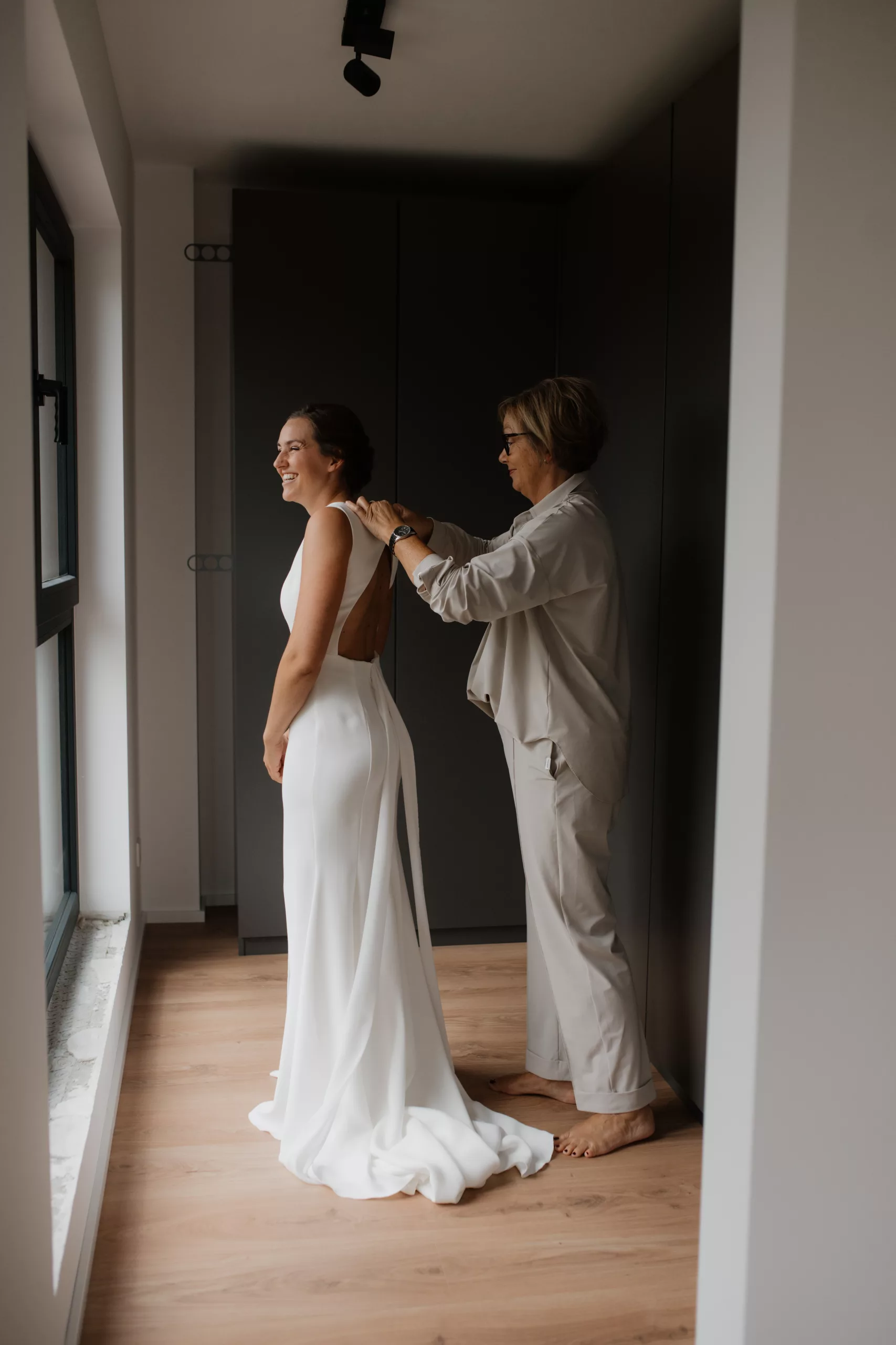 Braut und Mutter, Mutter hilft der Braut das Brautkleid anzuziehen