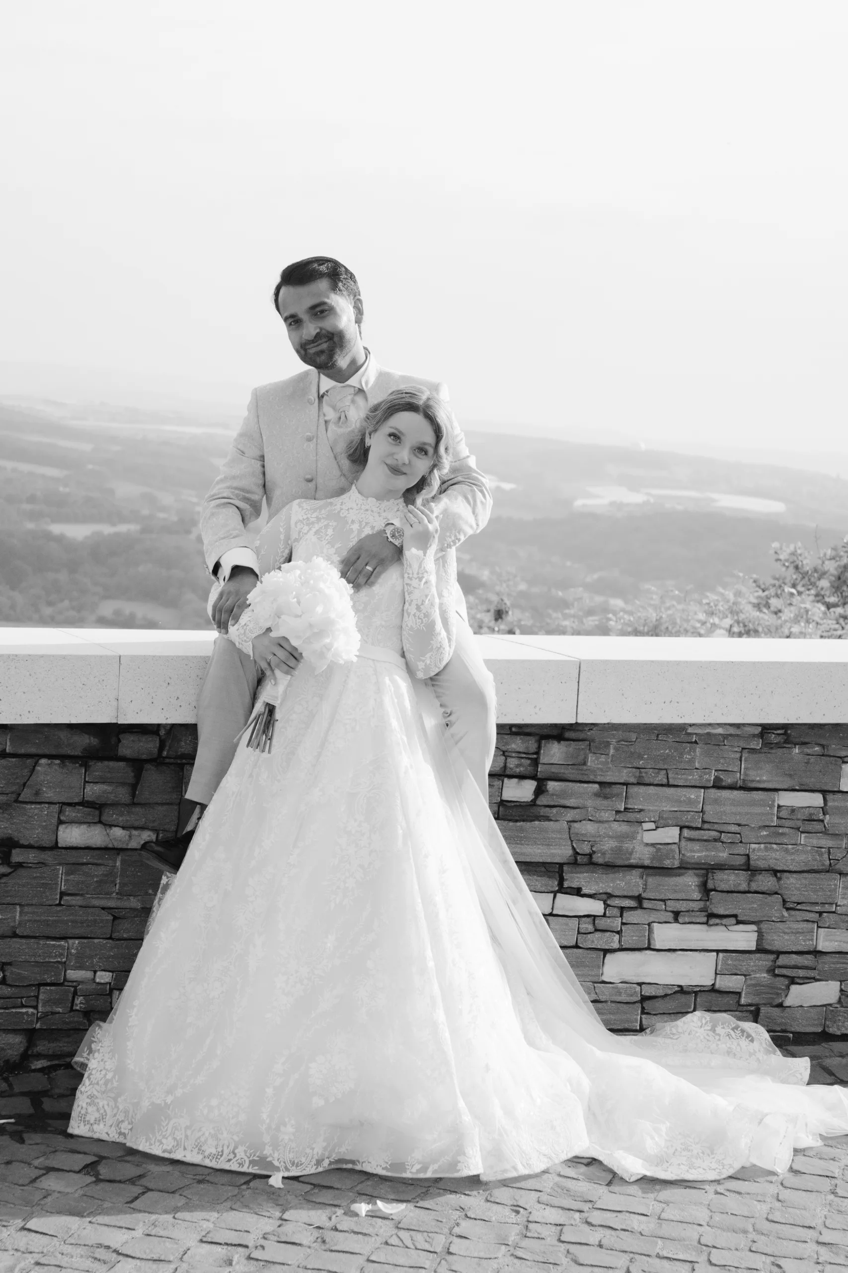 Hochzeitspaar umarmt sich von hinten und lächelt warm in die Kamera