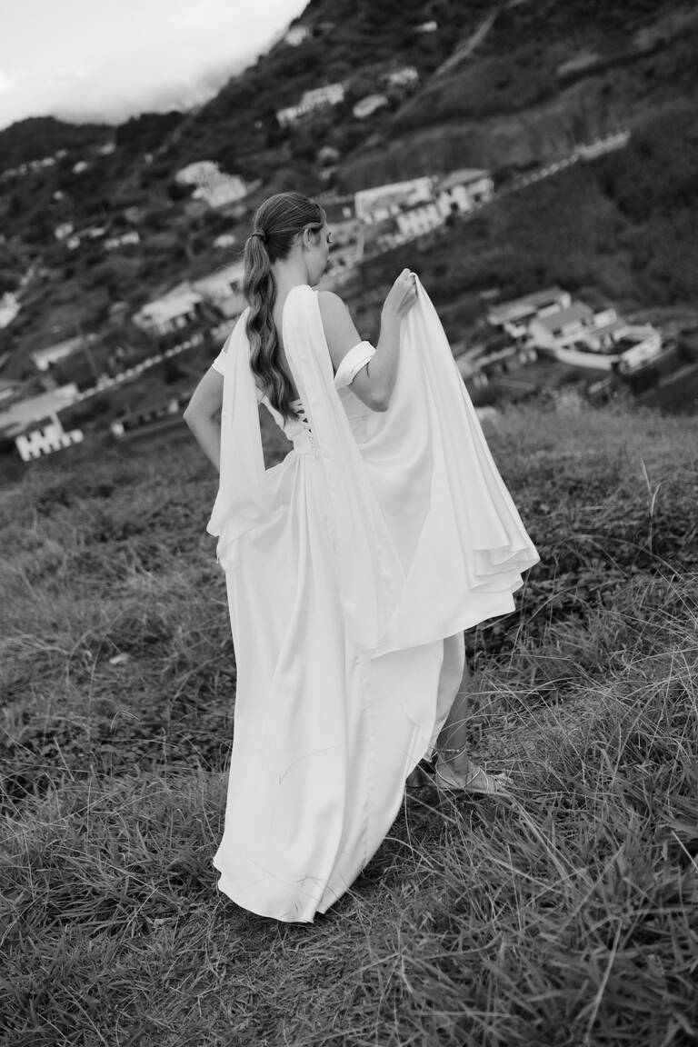 Braut hebt Kleid, editorial, steht vor dramatischer Kulisse in Madeira