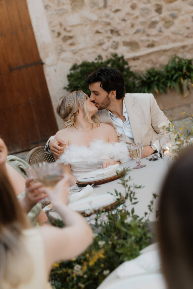 Hochzeitspaar liegt sich in den Armen und küsst sich, Abendstimmung von einem mit Blumen geschmückten Hochzeitstisch in einer Finca auf Mallorca, Son Burget Villa