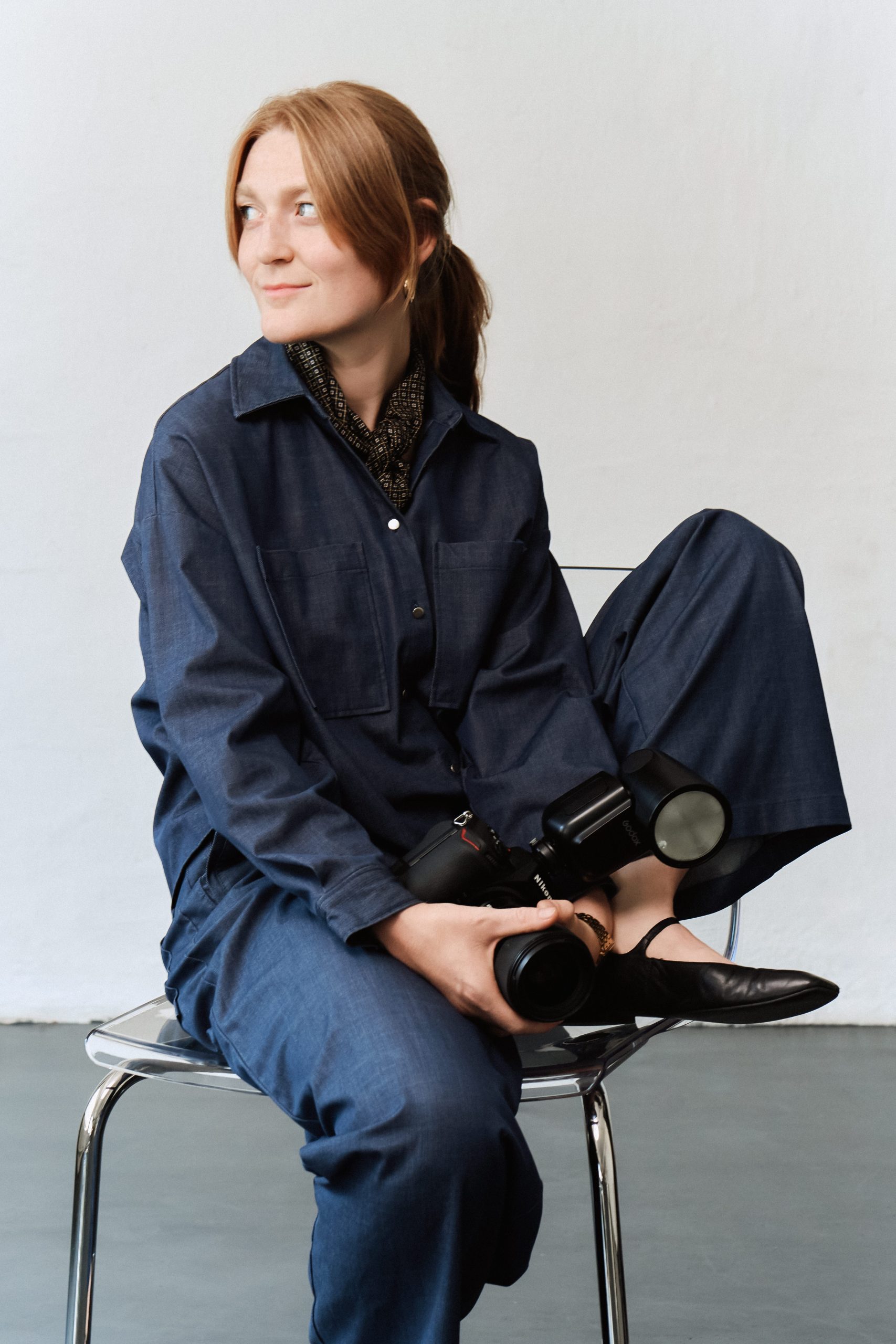Lea Feicks, Fotografin, auf einem Stuhl sitzend mit Kamera in der Hand